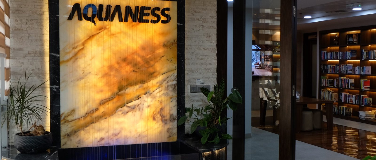 Reception at the Aquaness office in Dubai — backlit onyx water feature beside the reference library